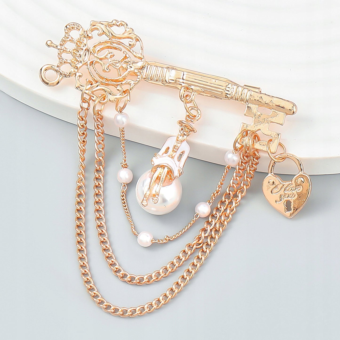 Agrafka - złota broszka z łańcuszkami, kluczem, kłódką i kobietą